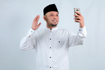 Happy asian muslim man holding and pointing on phone cellular over white background. Ramadan concept