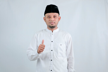 Asian Muslim man smiling to give greeting during Ramadan and Eid Al Fitr celebration over white background.