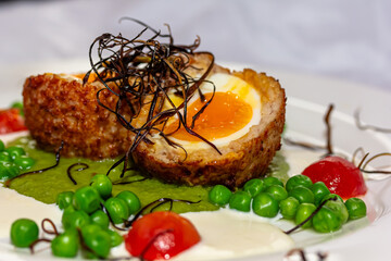 Fried egg Scottish eggs with green peas on a white plate in a restaurant