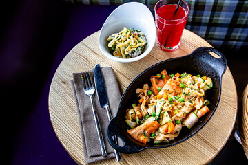 Fusilli pasta with chicken and vegetables in a black pan on a wooden table