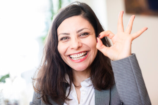 Smiling businesswoman sitting in an office making an ok sign