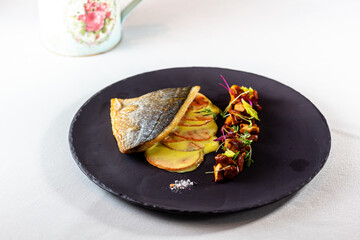 Grilled fish fillet with potato and vegetables on a black plate