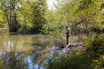 Fototapeta na wymiar Young fisherman fishing on the river bank surrounded by beautiful green nature, using small fish as bait on the hook. Sport and recreation concepts.