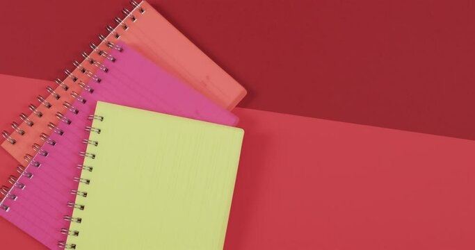 Overhead view of colourful notebooks with copy space on red background, in slow motion