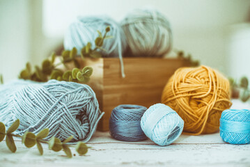 Close-up of Skeins of thread and wool in a wooden box on a table with foliage