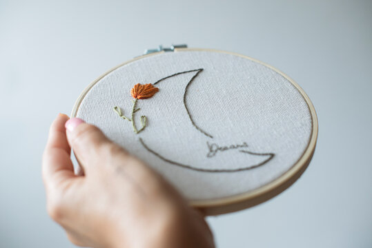 Woman's hand holding an embroidery hoop with a floral moon design