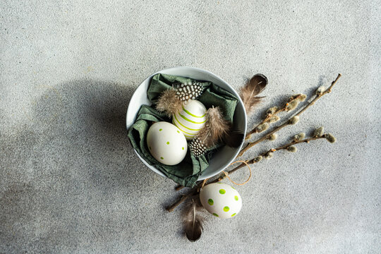 Overhead view of festive Easter arrangement with painted Easter Eggs, pussy willow branches and feathers in a bowl