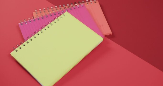 Overhead view of colourful notebooks on red background, in slow motion