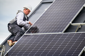 Man worker mounting photovoltaic solar panels on roof of house. Engineer in helmet installing solar module system with help of hex key. Concept of alternative, renewable energy.