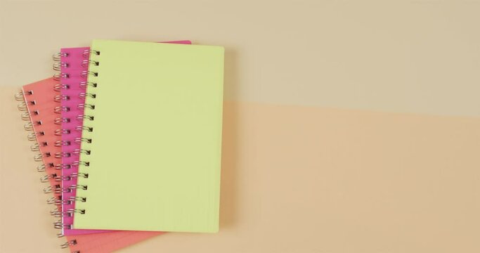 Overhead view of colourful notebooks with copy space on beige background, in slow motion