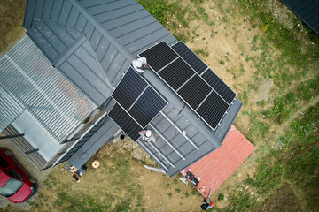 Builders building photovoltaic solar module station on roof of house. Men electricians in helmets...