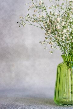 Close-up of a bunch of white Gypsophila flowers in a green glass vase on a table