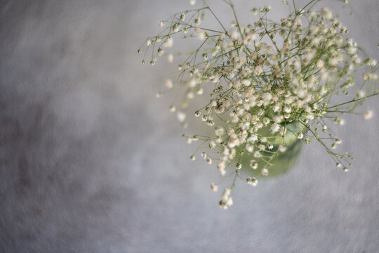 Overhead view of a bunch of  white Gypsophila flowers in a green glass vase on a table