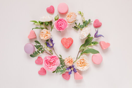 Overhead view of a Floral arrangement of roses, chrysanthemums, alstroemeria  flowers and foliage around heart shape candies on a pink background