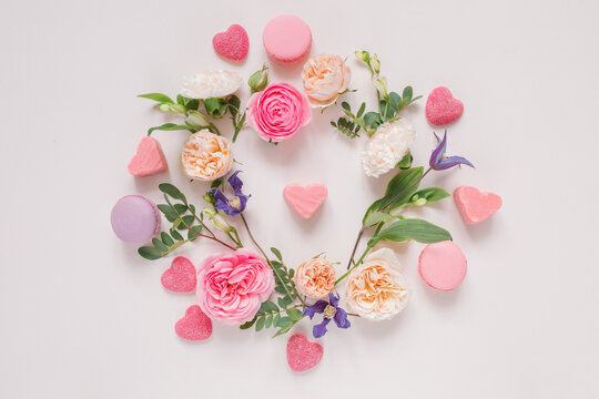 Overhead view of a Floral arrangement of roses, chrysanthemums, alstroemeria  flowers and foliage around heart shape candies on a pink background