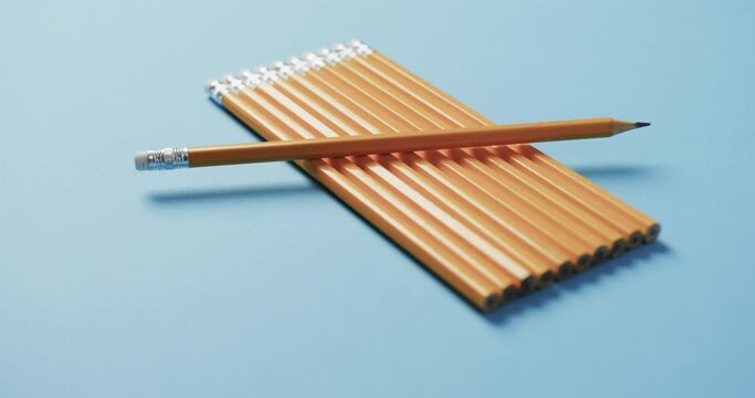 Close up of pencil on row of pencils with blue background, in slow motion