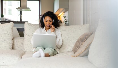Smiling young black woman freelancer working from home, sitting on couch, using laptop, copy space....