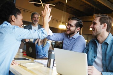 Successful business people giving each other a high five in a meeting. Two young business professionals celebrating teamwork in an office
