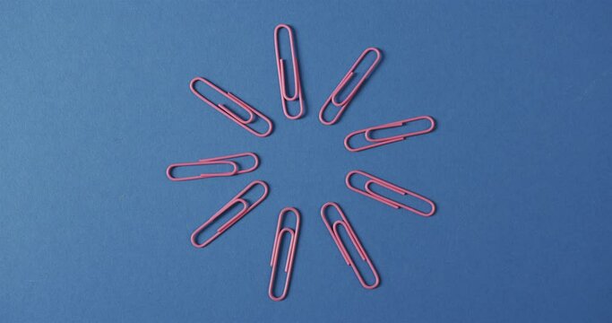 Overhead view of pink paper clips arranged on blue background, in slow motion