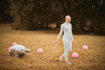 Portrait of young hairless girl with alopecia in white cloth walking tardigrade toy in fall park,...