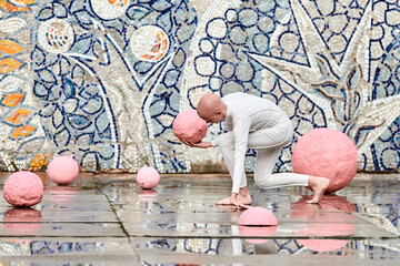Young hairless girl with alopecia in white futuristic suit dancing outdoor smoothly and takes pink ball on abstract mosaic Soviet background, symbolizes self expression and cultural identity