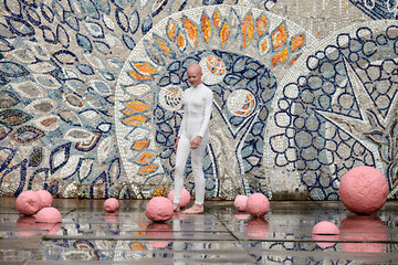 Young hairless girl ballerina with alopecia in white futuristic suit dancing outdoor among pink...