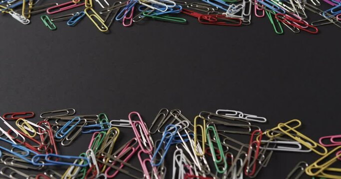 Close up of scattered colourful paper clips with copy space on black background, in slow motion