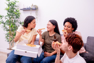 Diverse friends enjoying slices of pizza and beer bottles in a bright living room with a plant. 