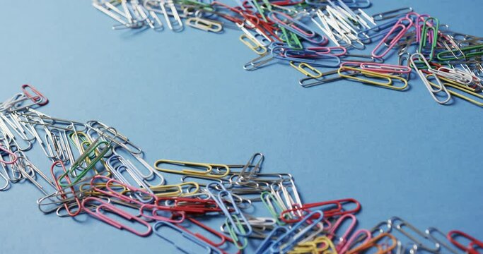 Close up of scattered colourful paper clips with copy space on blue background, in slow motion