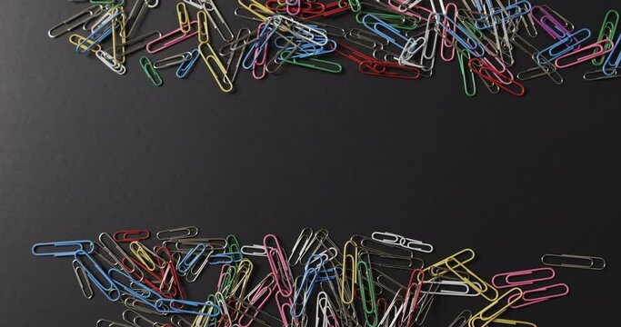 Overhead view of scattered colourful paper clips with copy space on black background, in slow motion