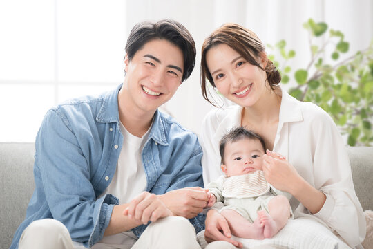 メインビジュアルにも！若い家族、パパと赤ちゃんを抱っこするママ　綺麗な部屋で幸せな家族のイメージ