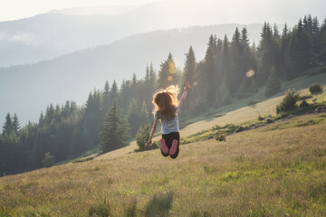 Happy little girl jumping and enjoying life at a spring meadow on the background of a picturesque mountain slopes. - 725488415