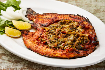 grilled Bulti fish with lemon slice, onion and salad served in dish isolated on table top view of arabic food