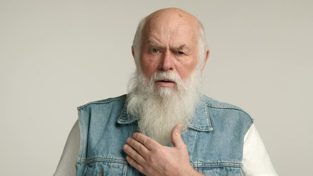 An elderly man coughs deeply, clutching his chest with a hand, a look of discomfort on his face, set against a plain background, indicating a potential health issue. Camera 8K RAW. 