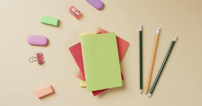 Overhead view of colourful notebooks with school stationery on beige background, in slow motion