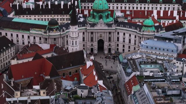 High angle of building roofs in urban borough. Tilt up reveal of Hofburg castle complex with palaces and towers. Vienna, Austria