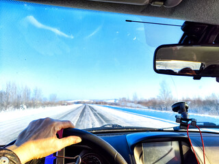 Hand of woman on the steering wheel in a car and view through the windshield of a winter road with...