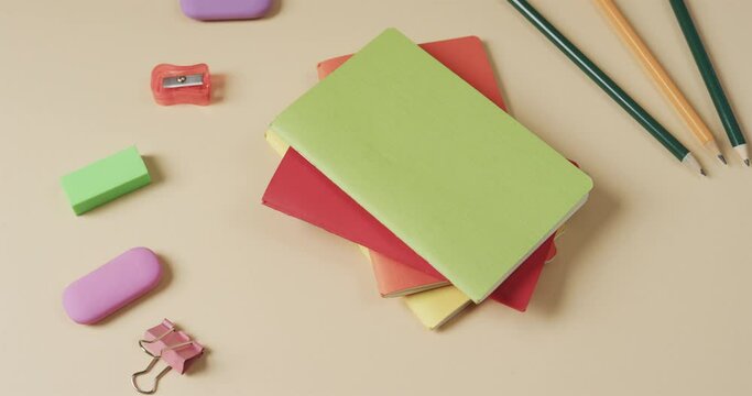 Close up of colourful notebooks with school stationery on beige background, in slow motion