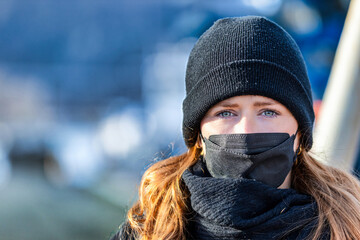 Woman with long red hair and a hat wears an FFP 2 protective mask.