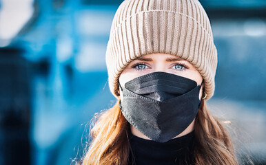 Woman with long red hair and a hat wears an FFP 2 protective mask.