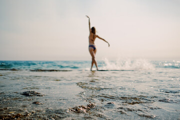 A woman with arms raised in a moment of freedom at the sunlit seashore, with gentle waves lapping...