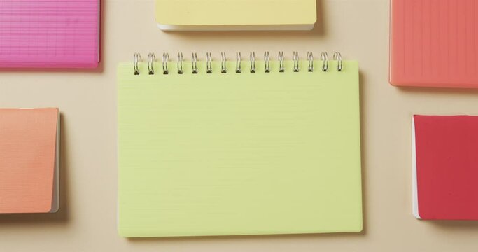 Overhead view of colourful notebooks arranged on beige background, in slow motion