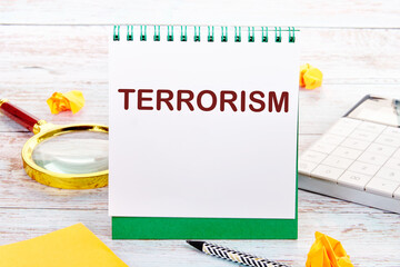 TERRORISM text on the white sheet of the notebook is next to a magnifying glass, calculator,...