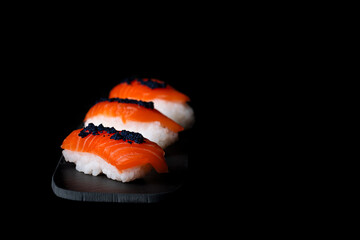 Taking delicious nigiri sushi on black plate and black background. Rice, salmon and caviar. Japanese food.