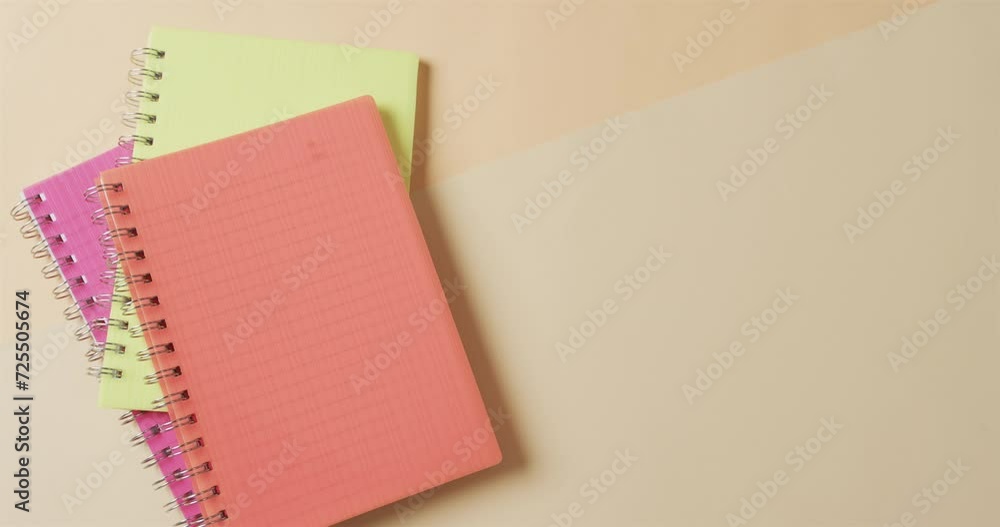 Poster overhead view of colourful notebooks with copy space on beige background, in slow motion