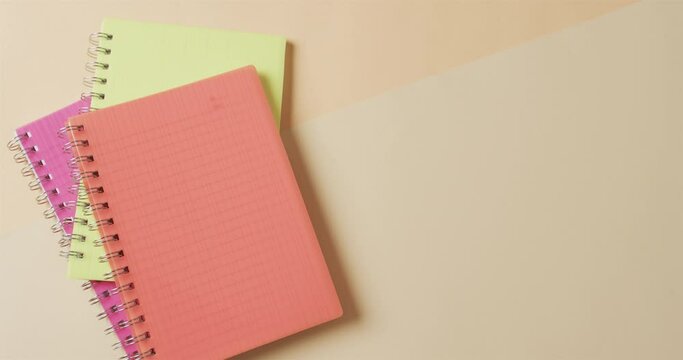Overhead view of colourful notebooks with copy space on beige background, in slow motion