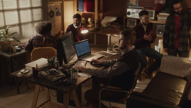 Lowkey shot of ethnically diverse group of tech lovers creating software startup together, brainstorming and program coding in 90s style garage office