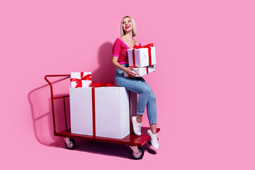 Full length photo of dreamy woman hold gift boxes sit on shopping cart with large present look...