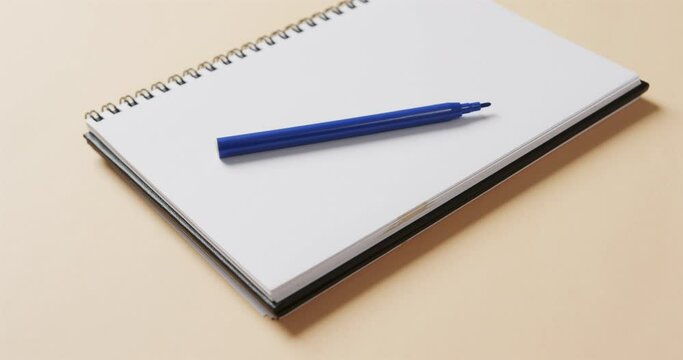 Close up of blue marker on notebook with beige background, in slow motion