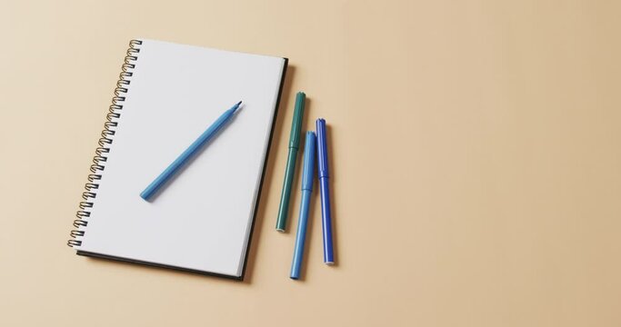 Close up of blue markers with notebook with copy space on beige background, in slow motion